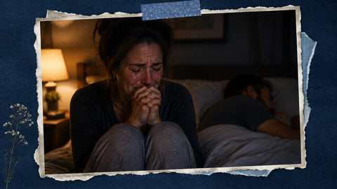 A mother sits up in bed late at night, hands clasped tight in anguished prayer, tears on her cheeks, while her husband sleeps